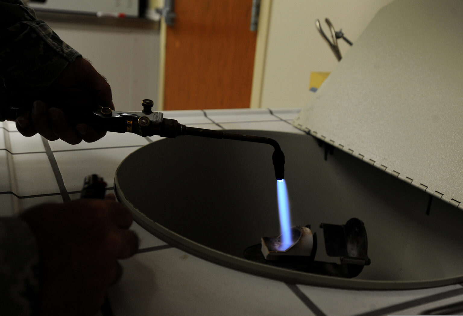 Dental lab technician using a torch to melt gold alloy while casting a crown restoration