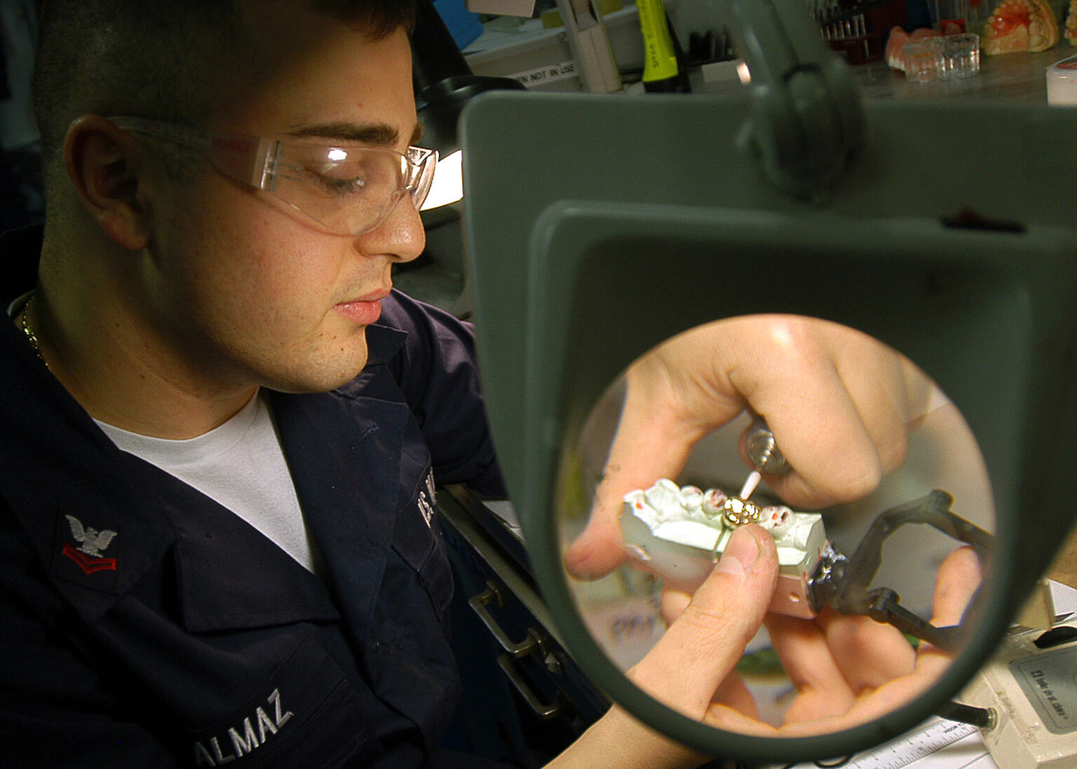 Dental lab technician examining a crown restoration through a magnifying lamp